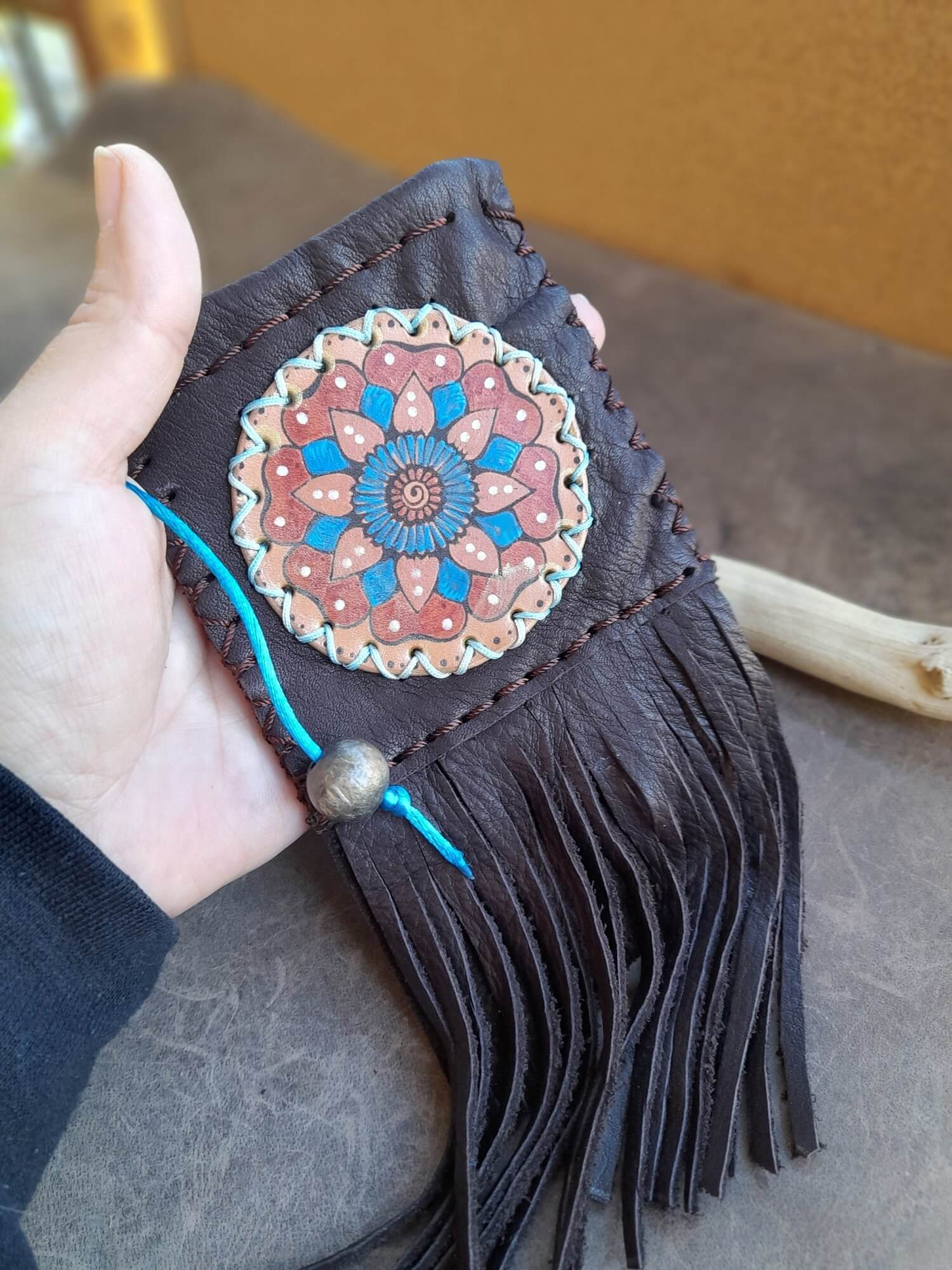 Hand holding a decorative leather item with a mandala design and fringes.
