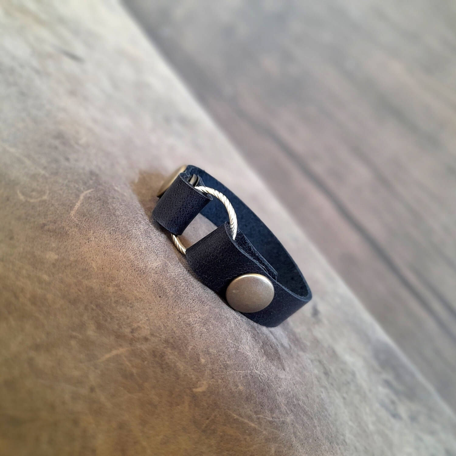 Handmade black full grain leather ring holder bracelet displaying a gold wedding band.