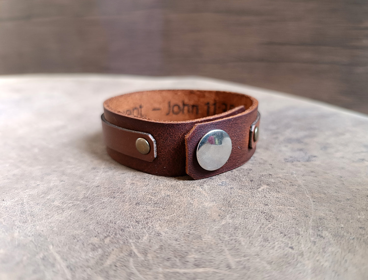 Layered brown leather cuff with rose gold cross charm and customizable underside for engraving Bible verses or personal messages.