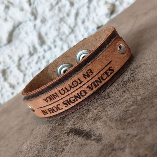 In Hoc Signo Vinces bracelet flat view showcasing engraving and snap closures, photographed on a textured surface.