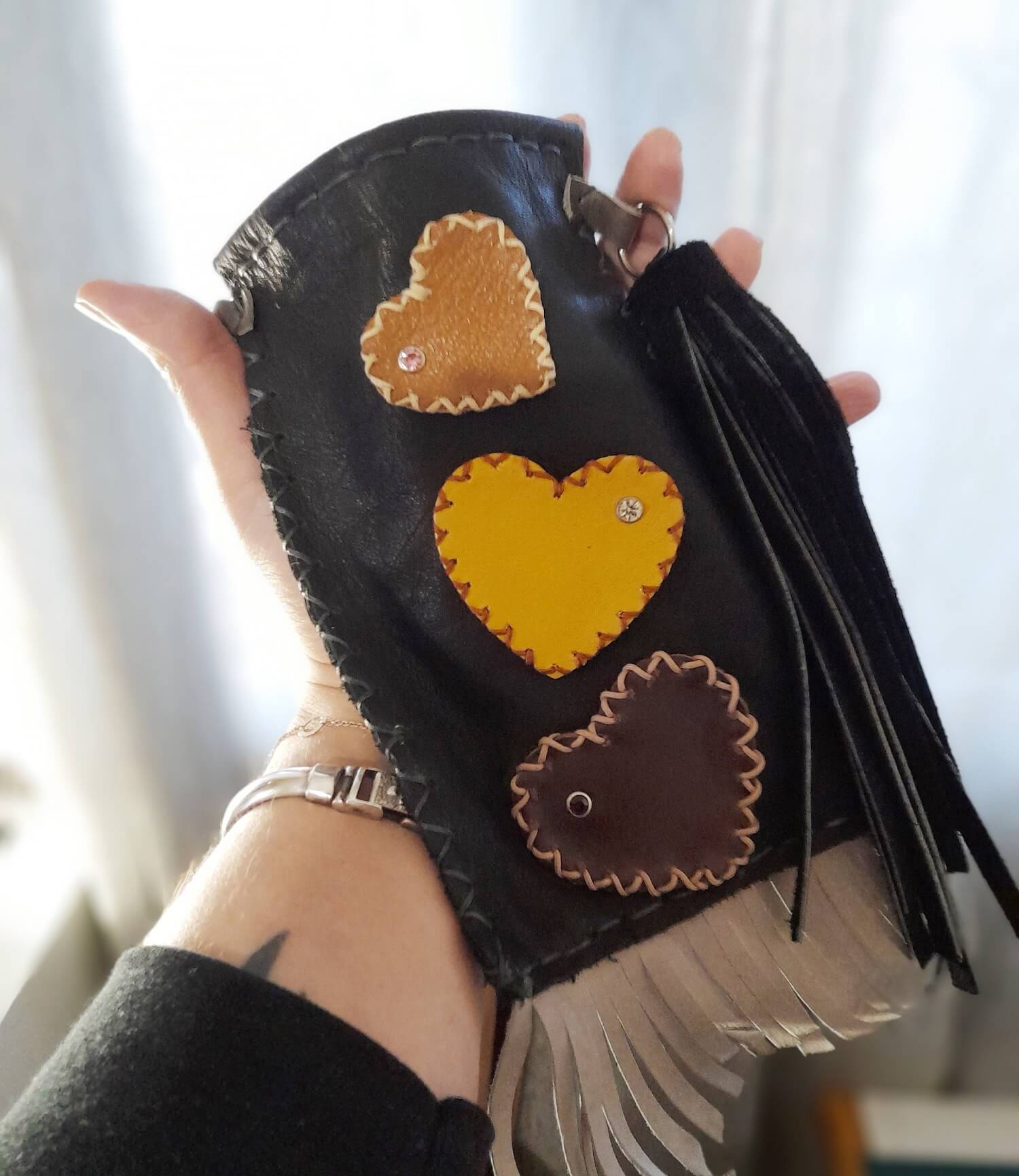 Leather phone bag with hearts held on hand, demonstrating fit and size.