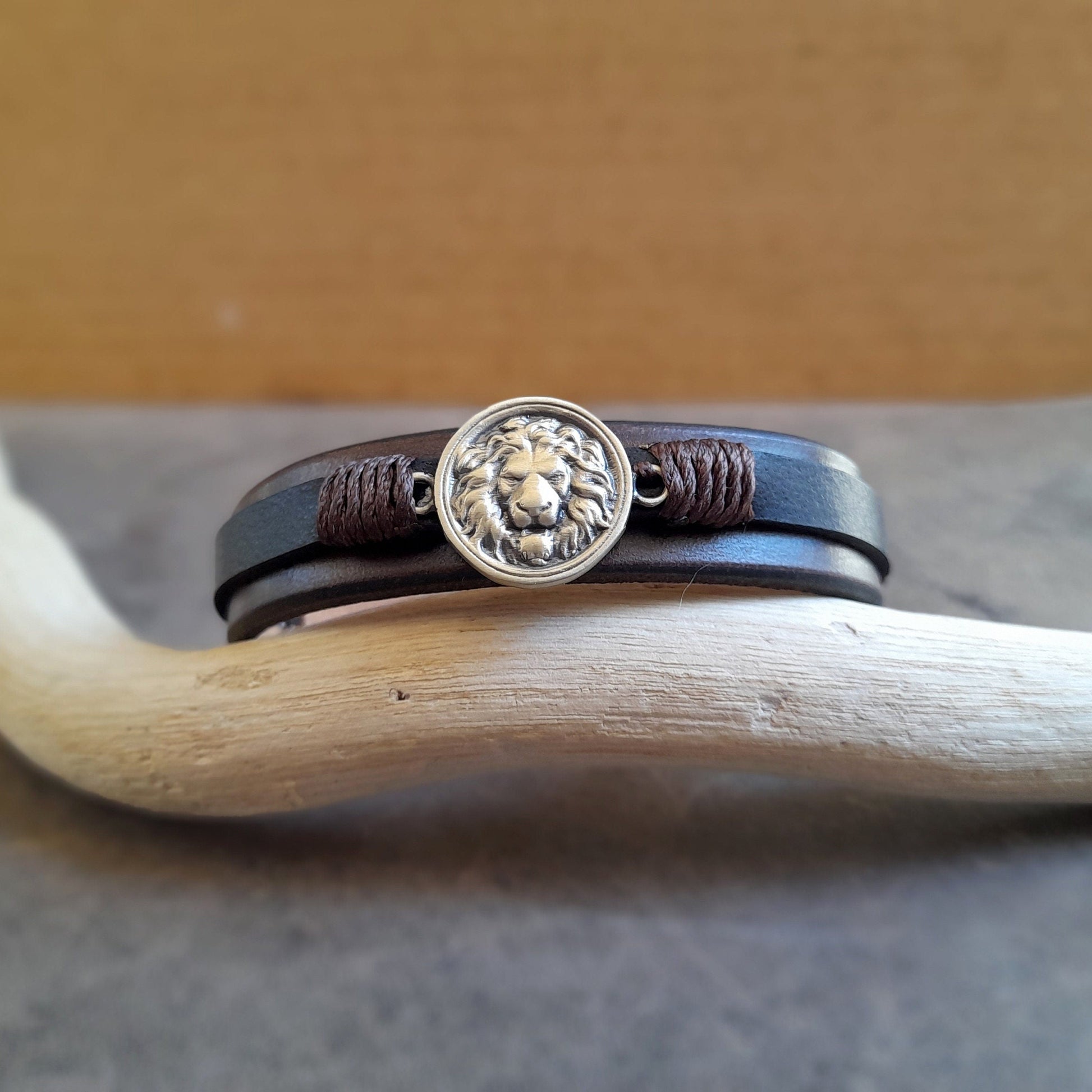 Lion Leather Bracelet, showing layers of chestnut brown and black full-grain leather, tarnish-free brass pendant and snap button closure.