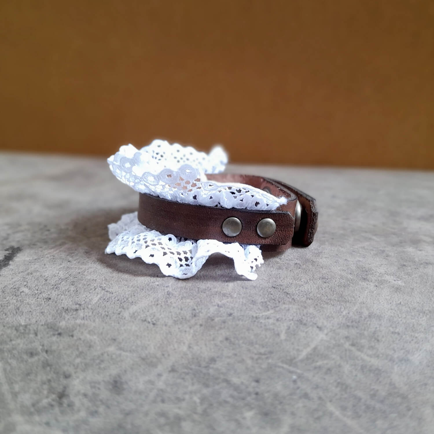 Side View close up of The Prairie Lace Cuff, a hand-dyed dark brown Crazy Horse leather bracelet. Features delicate lace peeking out, adorned with antique bronze stud rivets, and visible snap button closure.