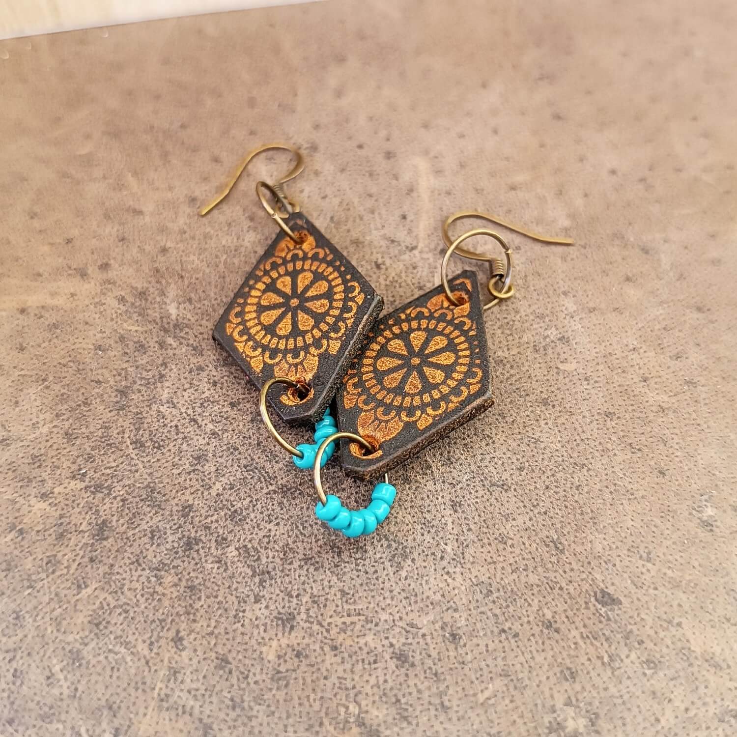 Pair of earrings with engraved mandala and brown design on a beige background