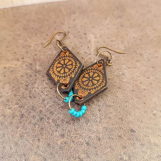 Pair of earrings with engraved mandala and brown design on a beige background