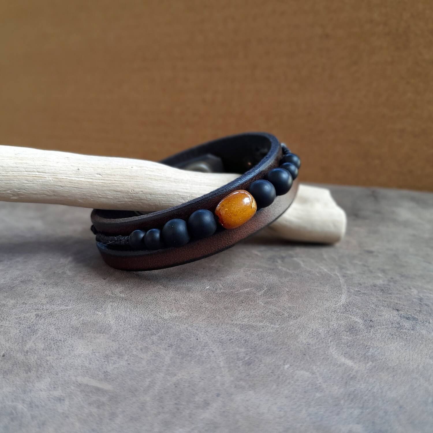 Men's chestnut brown leather bracelet with matte black onyx beads and an amber barrel bead.
