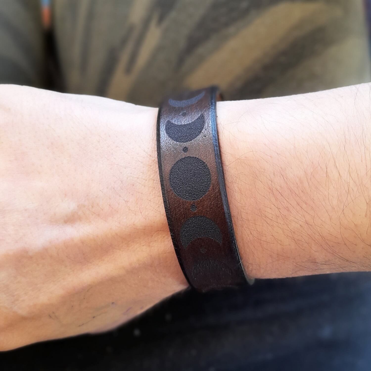 Brown leather bracelet with black moon phases on a wrist showcasing genderless style