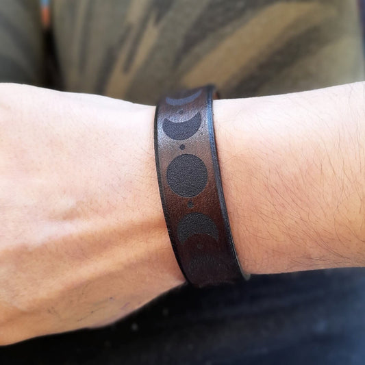 Brown leather bracelet with black moon phases on a wrist showcasing genderless style