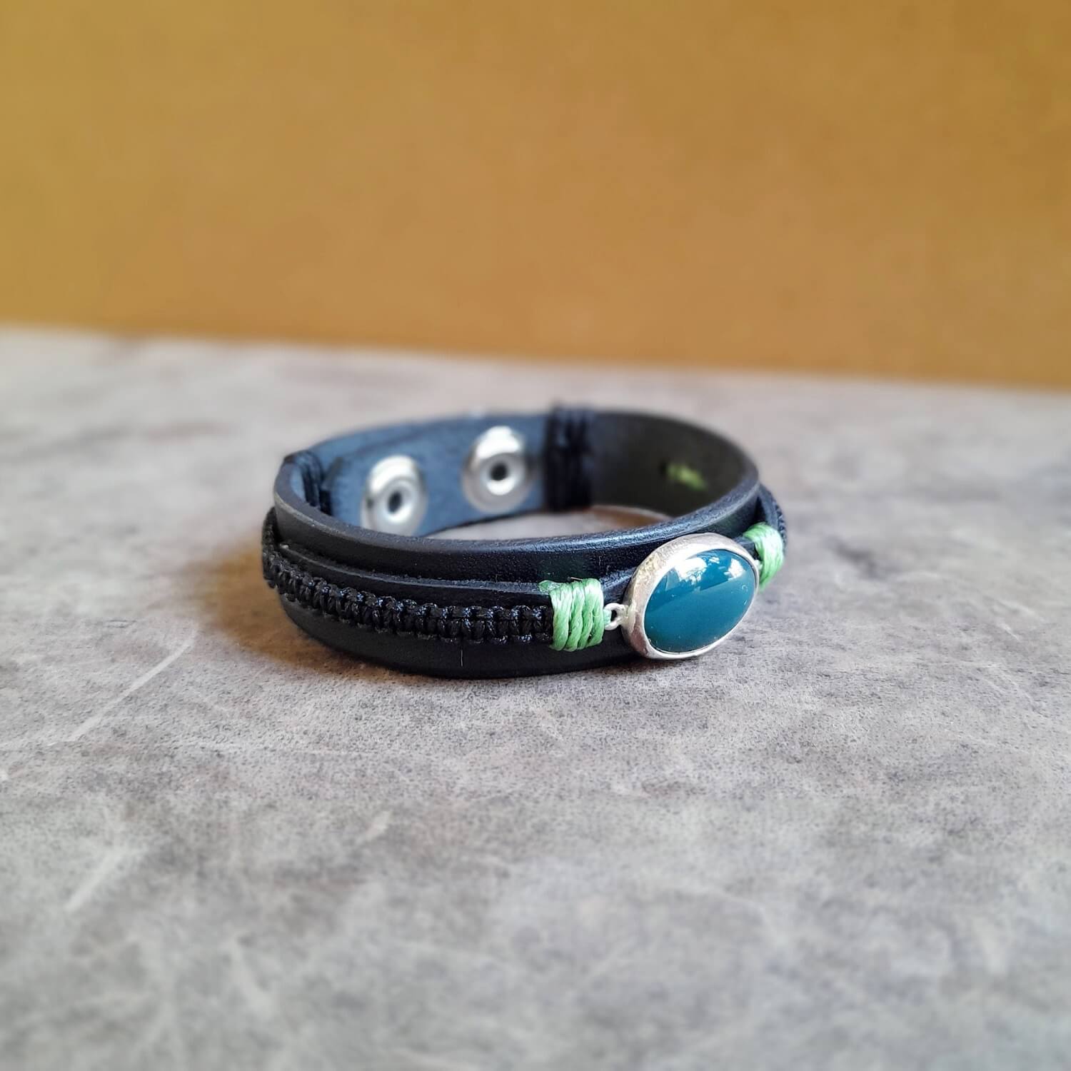 The OOAK Green Aventurine Black Leather Bracelet side view: A layered black Vachetta leather cuff with black macramé, featuring a prominent natural dark green Aventurine stone set in a sterling silver pendant.