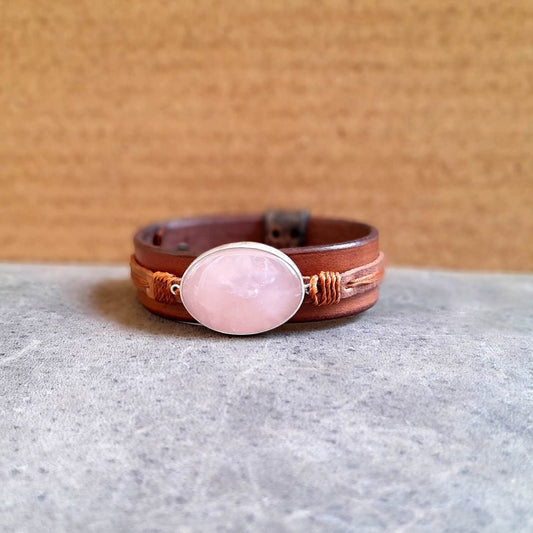 The OOAK Large Rose Quartz Leather Cuff: A wide, layered oiled Vachetta and brown cowhide leather bracelet featuring a prominent oval natural rose quartz stone set horizontally on a sterling silver pendant, wrapped with warm brown cord.