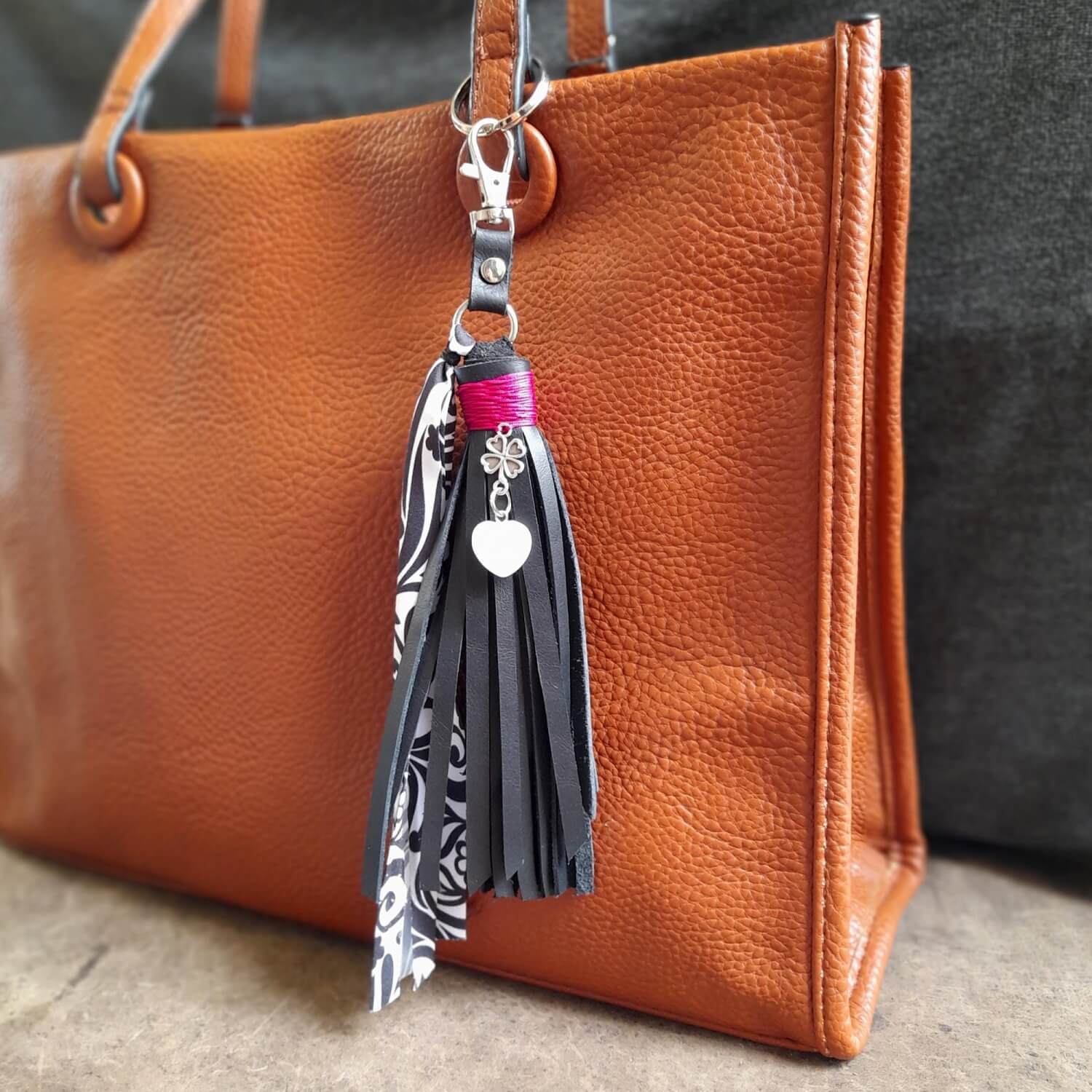 OOAK Moonstone Heart Charm with a black suede leather tassel, attached on a brown leather bag. Features a natural Moonstone heart pendant, a silver four-leaf clover, and an abstract floral black and white fabric ribbon.