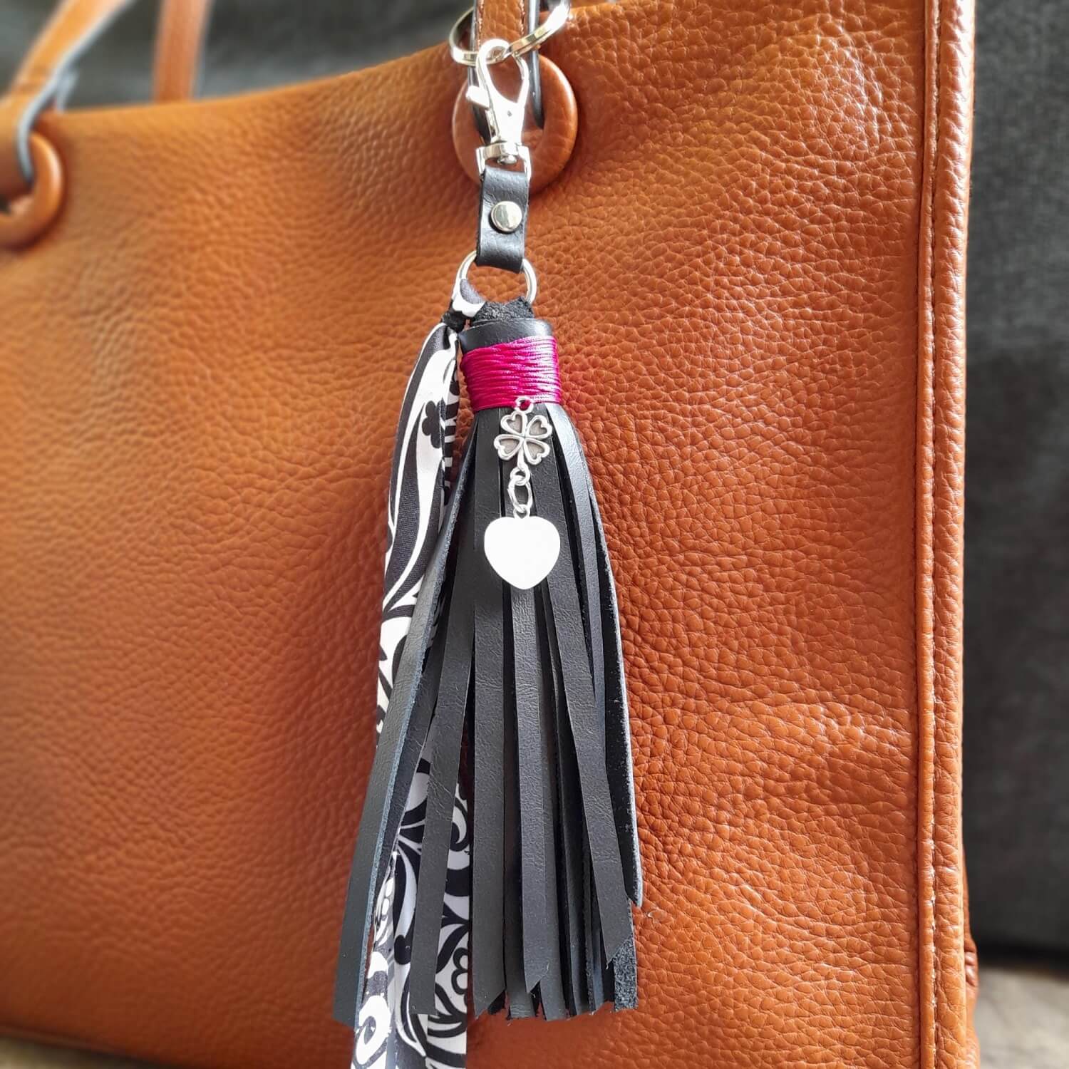 OOAK Moonstone Heart Charm with a black suede leather tassel on a bag (close up view). Features a natural Moonstone heart pendant, a silver four-leaf clover, and an abstract floral black and white fabric ribbon.
