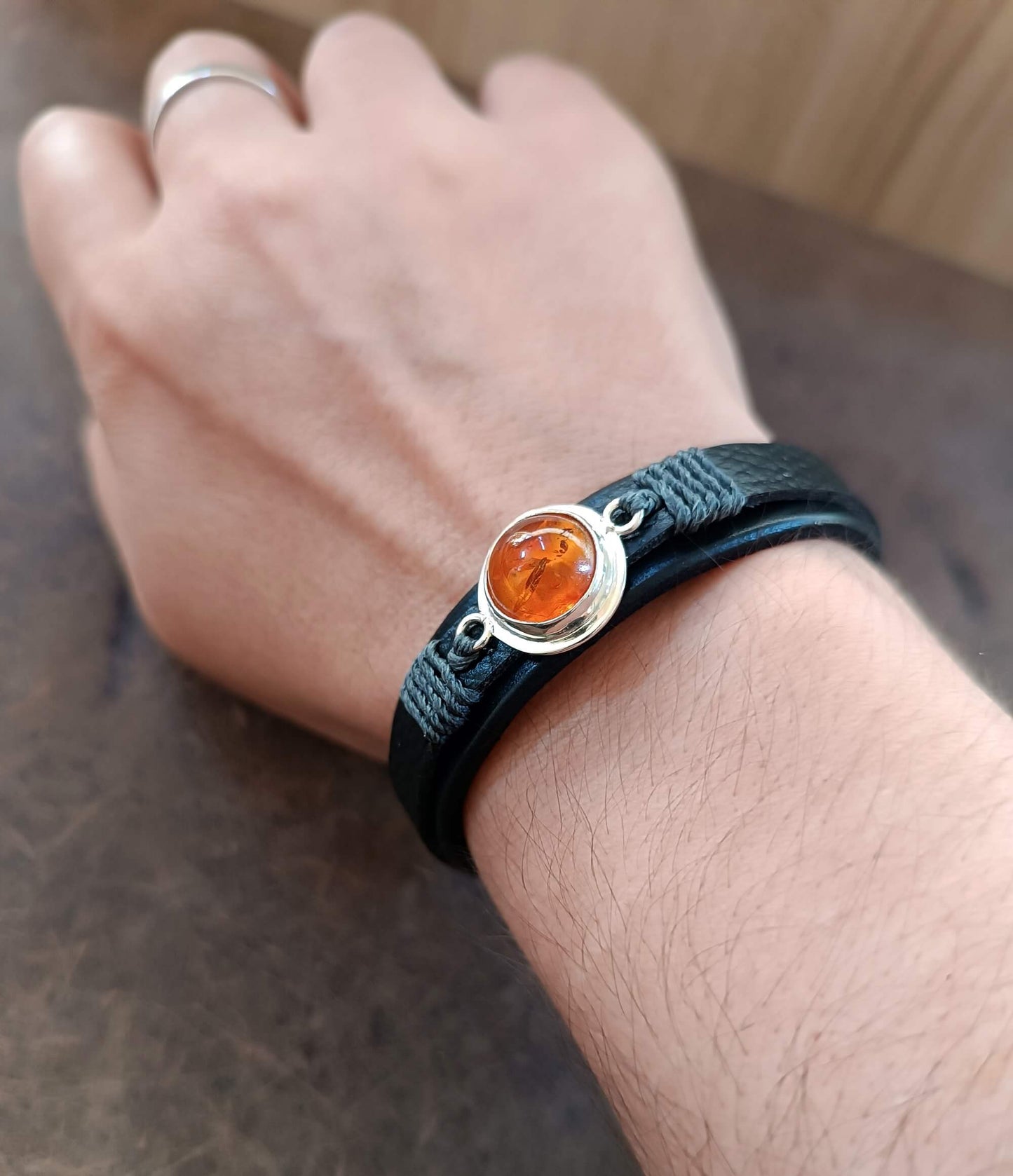 Hand wearing a black leather bracelet with greek amber stone and silver clasp on a neutral background