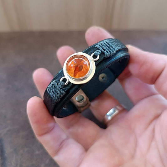 Black leather bracelet with amber stone held in a hand.