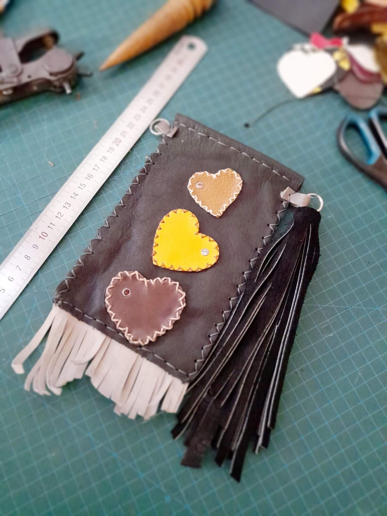 On the making: Hand-cut and hand-stitched leather phone bag in dark brown sheepskin with applied leather hearts and a long black suede tassel.