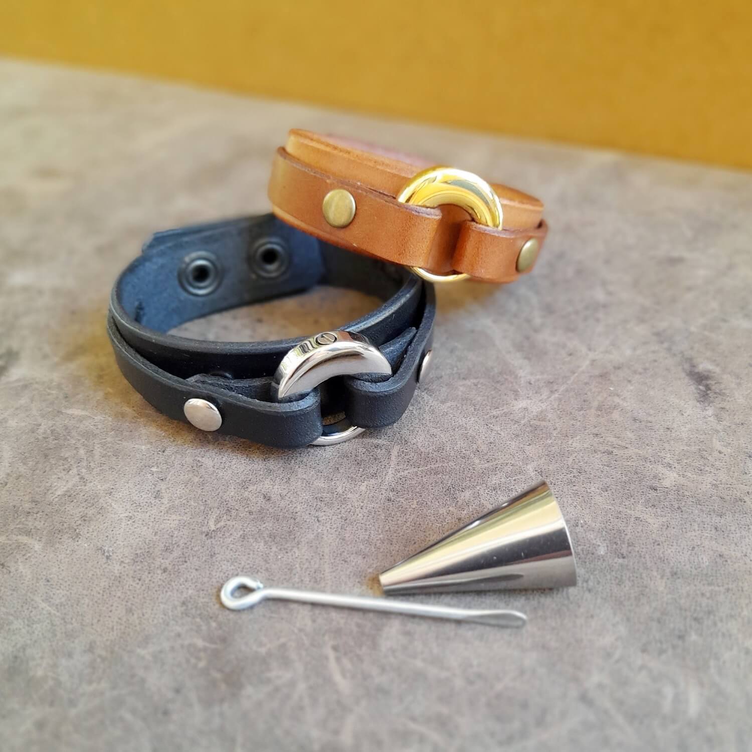 The black and brown cremation leather cuffs with urn pendants, along with their extra accessories: a little funnel and a scoop.