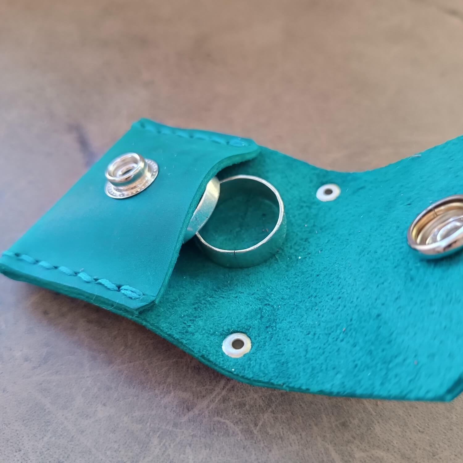 the petrol blue leather ring holder pouch open, showing that it carries two wedding bands.