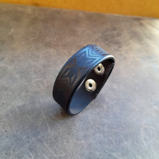 A Polynesian Tribal Bracelet made of full grain leather, hand dyed in dark brown and black, with a visible engraved pattern.