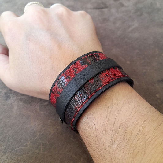 Hand wearing a red and black patterned leather bracelet on a neutral background
