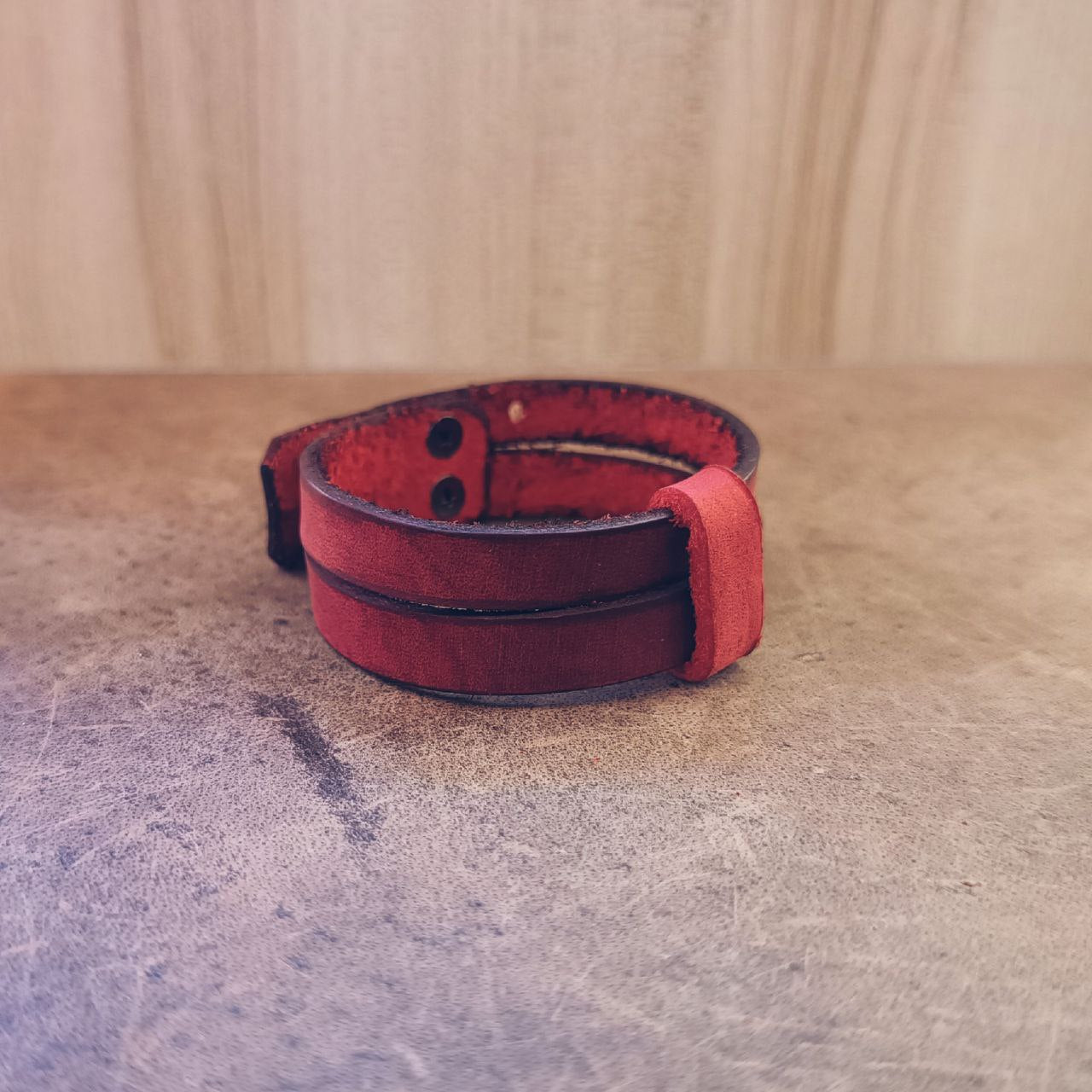 Red leather collar cuff side view on a textured surface with a wooden background.
