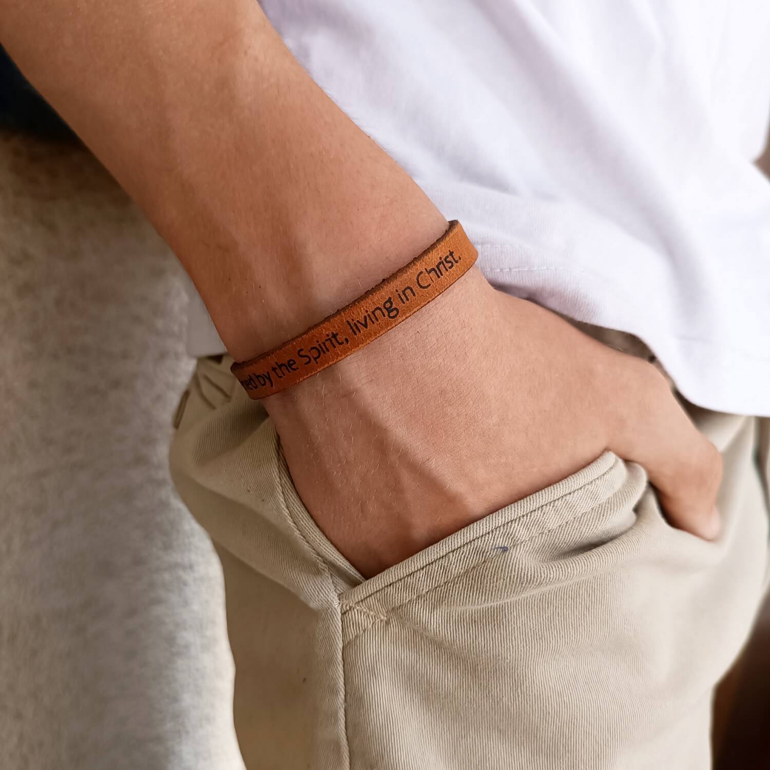 Young man wearing a minimalist brown leather bracelet with religious message.