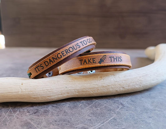Two brown leather bracelets with engraved text on a wooden surface.
