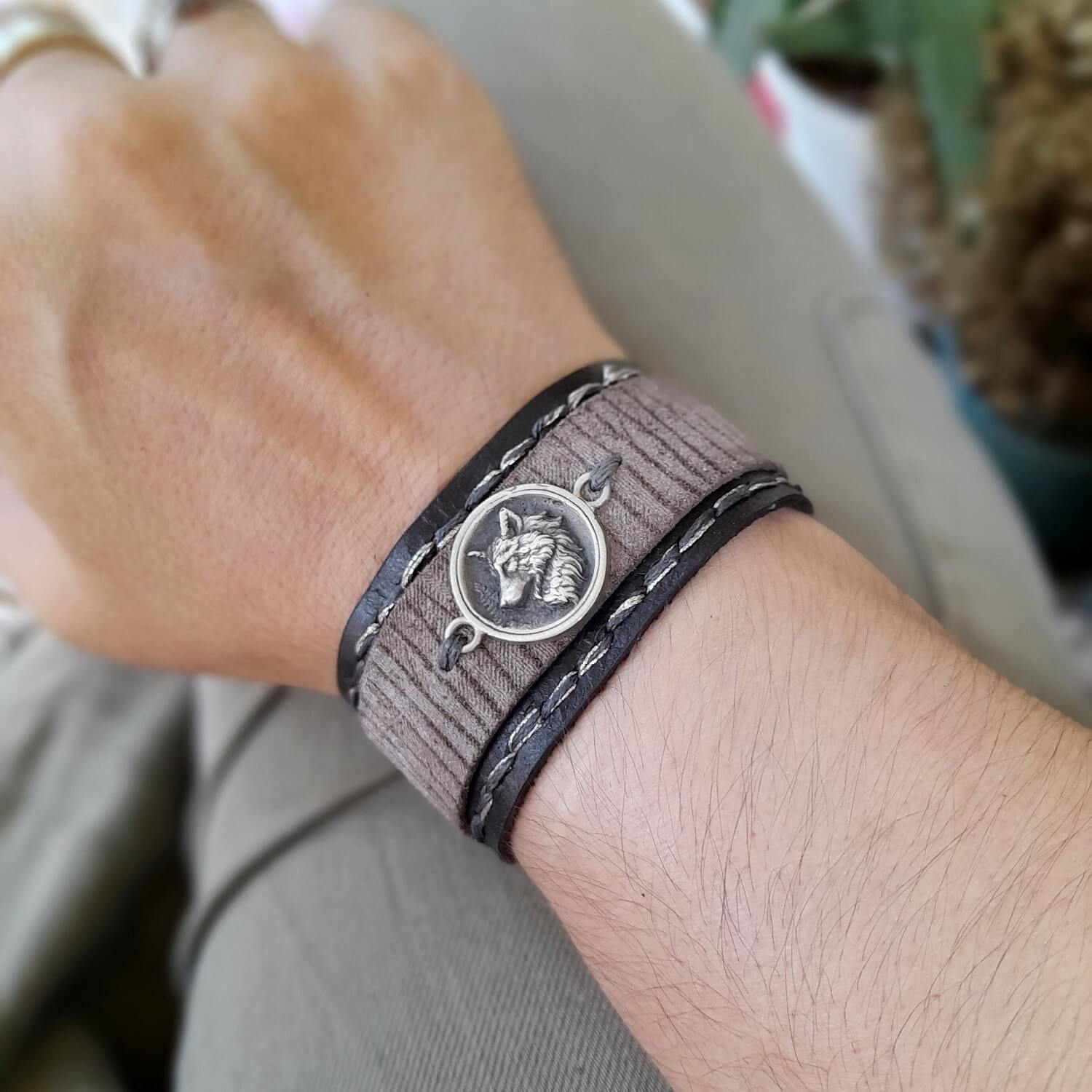 Close-up of a wrist wearing a black leather bracelet with a wolf pendant.