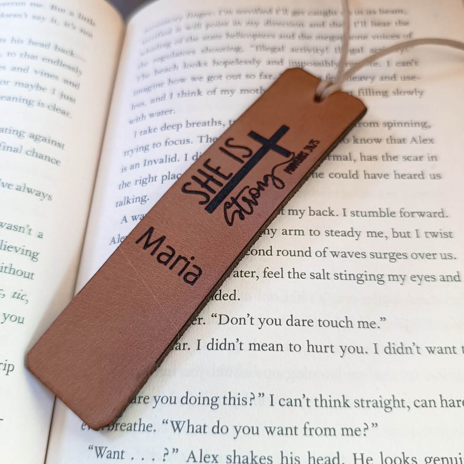Brown leather bookmark with 'She is Strong' and 'Maria' text on an open book.