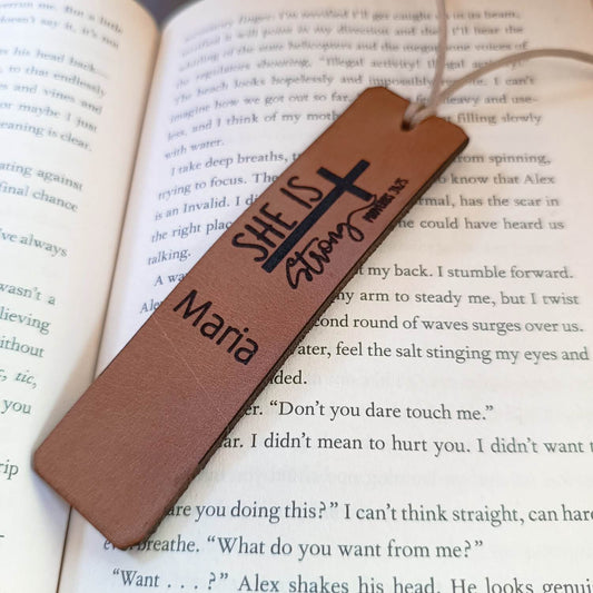 Brown leather bookmark with 'She is Strong' and 'Maria' text on an open book.