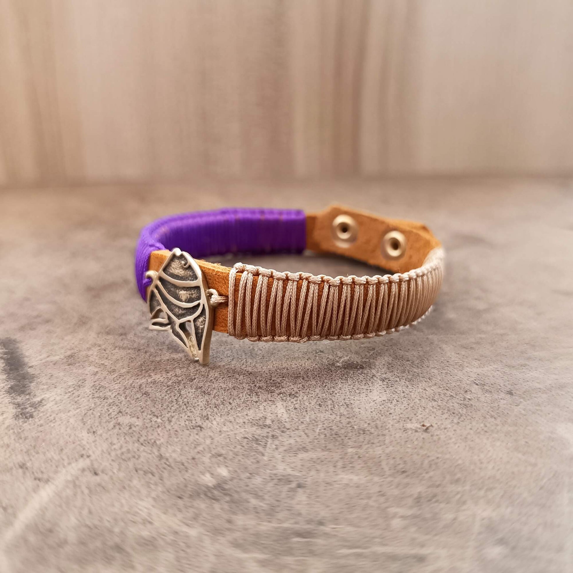 Bracelet with purple end and brown leather strap featuring a fish charm on a textured surface.