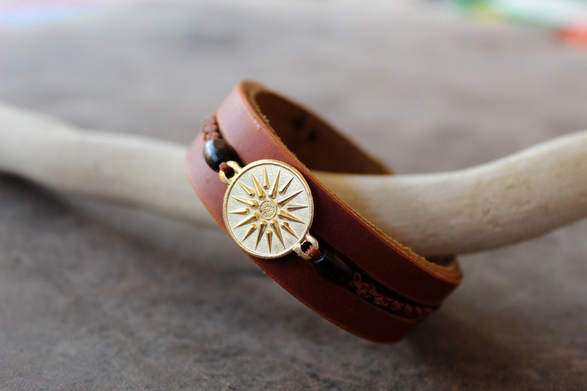Side view of Gold Vergina Sun Leather Bracelet, showing three layers of brown leather, hand-stitching, wooden beads, and macrame.