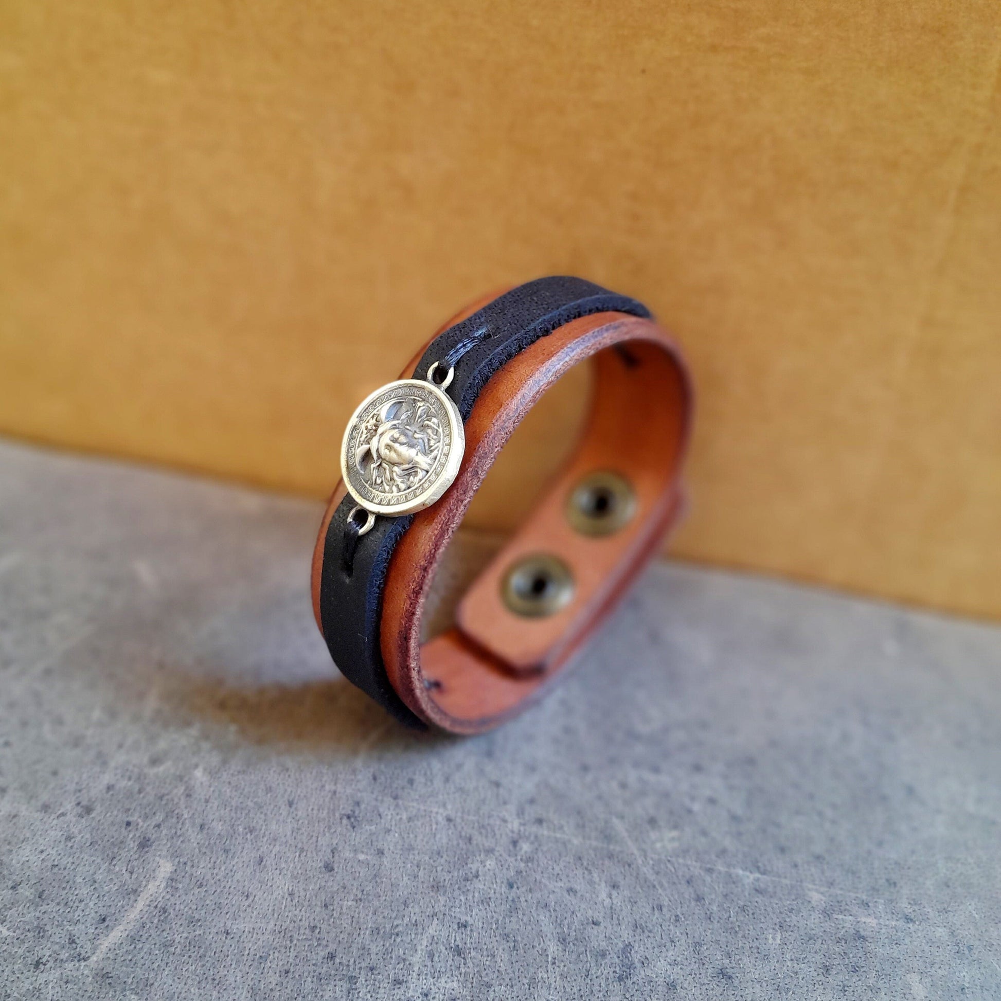 Side view of Greek Medusa Leather Bracelet, showing thickness of brown Crazy Horse leather, black stripe, and brass Medusa charm.
