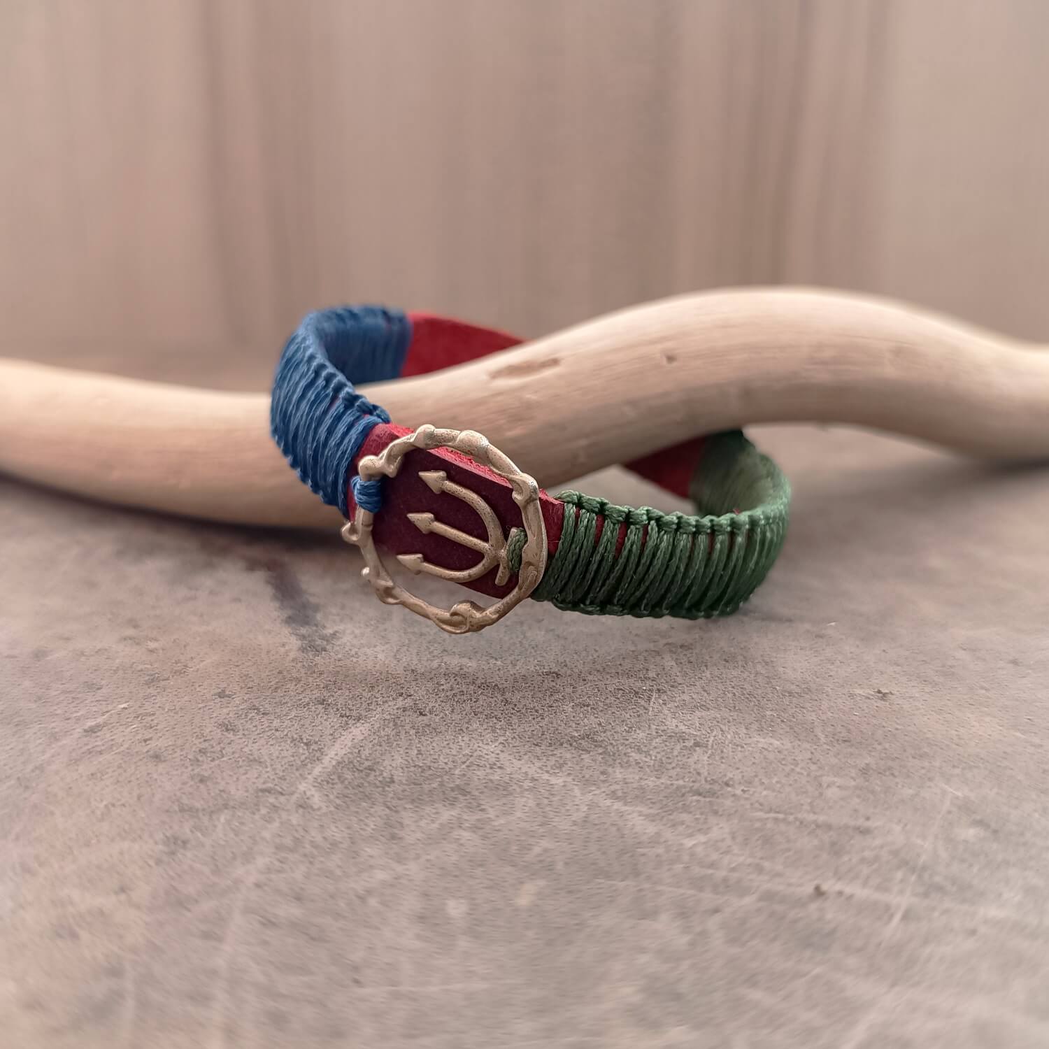 Side view of The Guardian's Balance Trident Bracelet, showing the thickness of the vibrant red Crazy Horse leather band and the intricate deep forest green and navy blue macrame knotting.