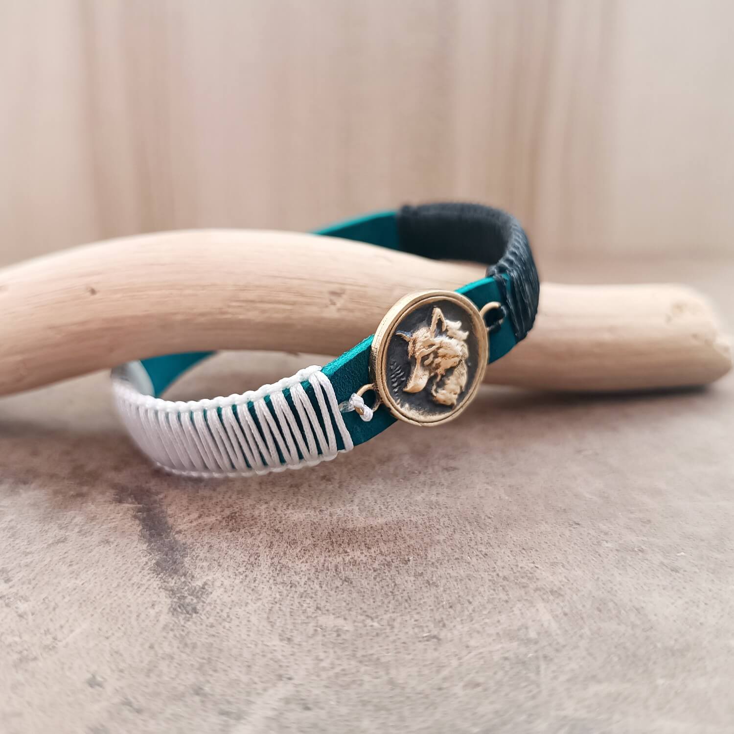 Side view of The Instinctive Shield Wolf Bracelet, showing the thickness of the blue Crazy Horse leather band and the intricate white and black macrame knotting.