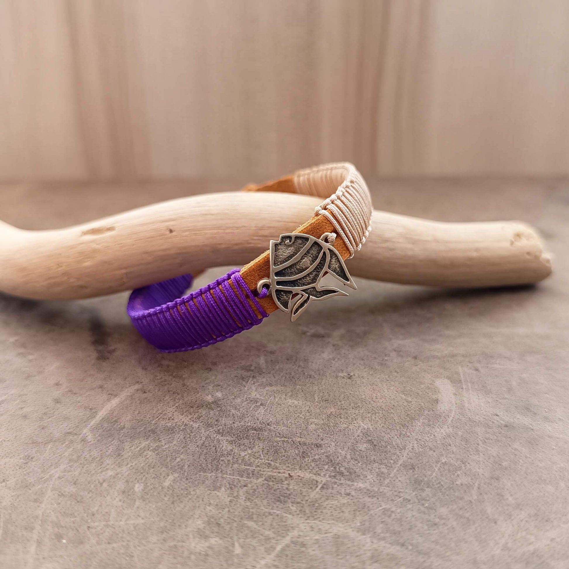 Bracelet with purple and bronze cord leather band and silver koi fish charm on a wooden stick