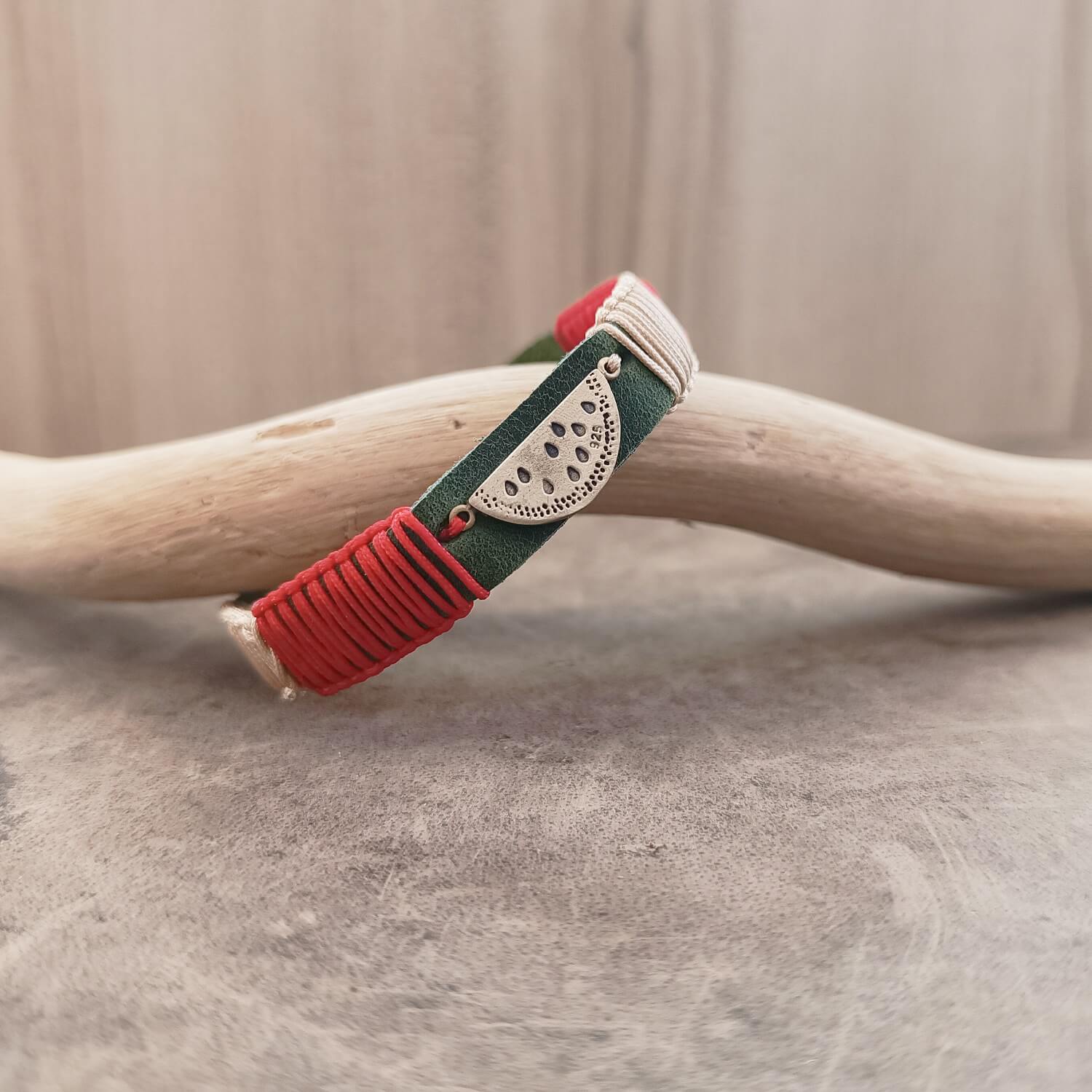 Side view of The Sweet Abundance Watermelon Bracelet, showing the thickness of the deep forest green Crazy Horse leather band and the intricate red and light bronze macrame knotting.