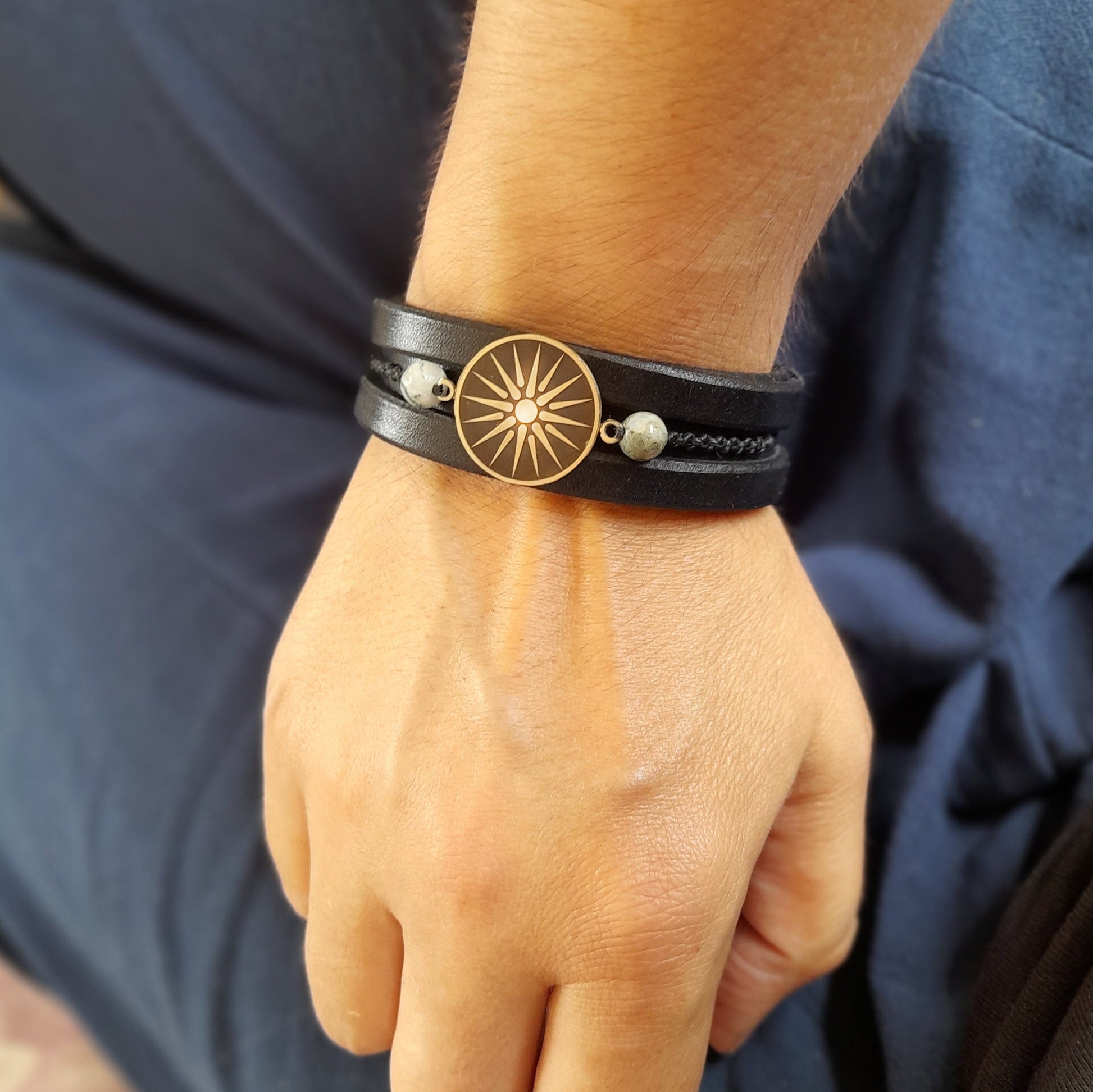Silver Vergina Sun Black Leather Bracelet worn on a wrist, showing the silver charm against black leather. Handcrafted by Lucky Seven Leather.