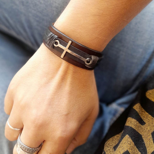 The Steadfast Spirit Cross Bracelet in brown - black version, worn on a woman's wrist, showcasing its bold horizontal stainless steel silver cross and the durable full-grain leather, adding a strong, masculine touch.