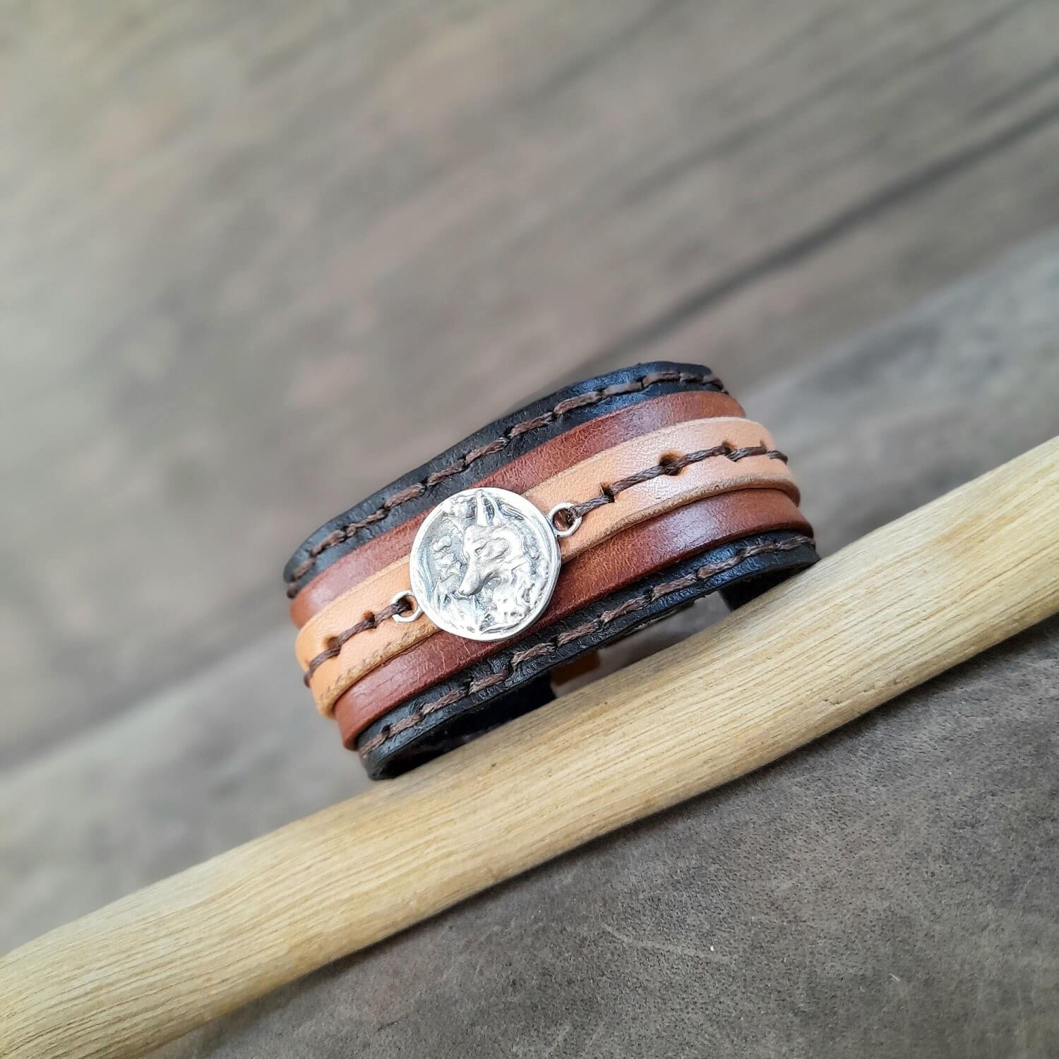 Multi-layered leather bracelet with a fox charm on a wooden stick against a wooden background