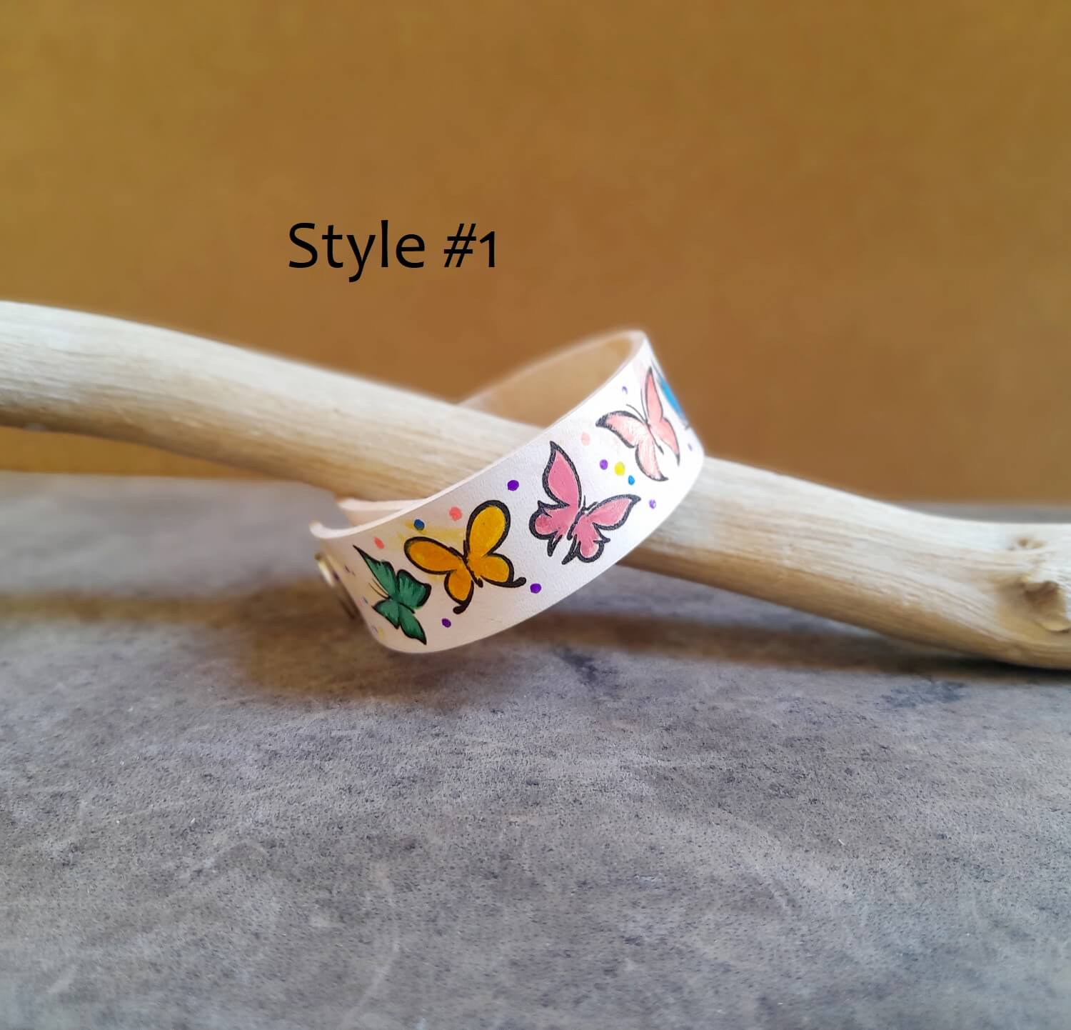 Wristband with butterfly designs on a wooden stick against a brown background - Style #1