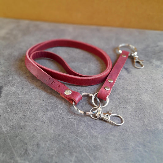 The Adapt Lanyard in Burgundy Red, showing the full length with the removable extension attached. Features personalized engraving/stamping, full-grain oiled vachetta leather, and heavy-duty brass hardware with a stainless steel lobster clasp.