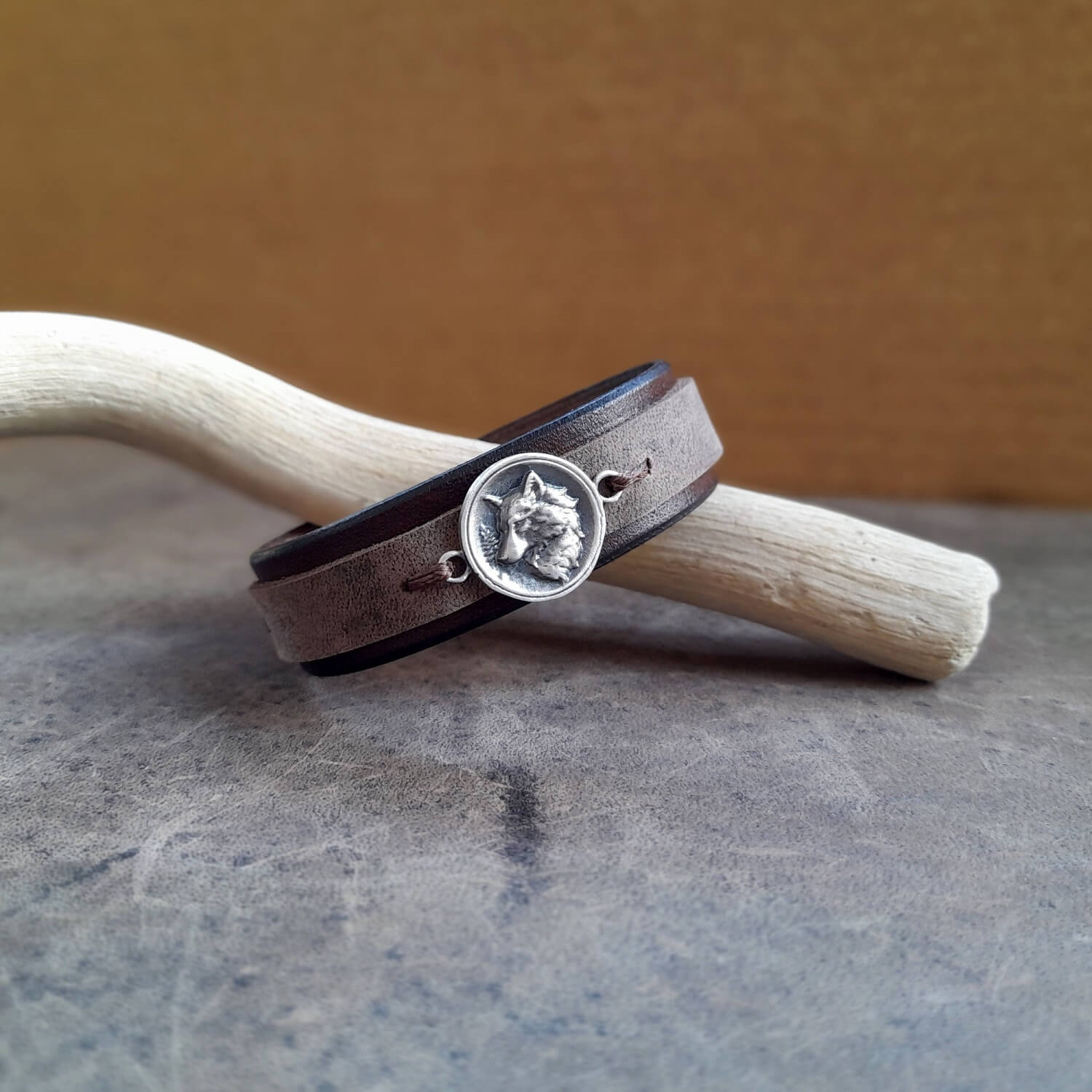 The Arctic Wolf Leather Bracelet: A layered chestnut brown and charcoal full-grain leather cuff featuring a prominent antique silver 925 white wolf pendant.