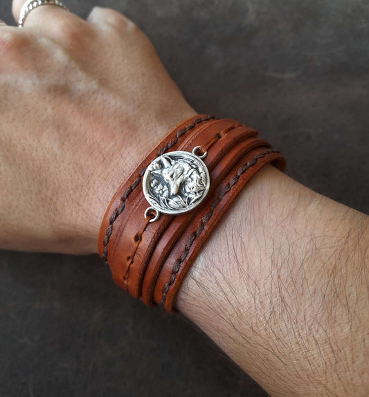 Brown leather bracelet with a silver fox charm on a wrist against a dark background