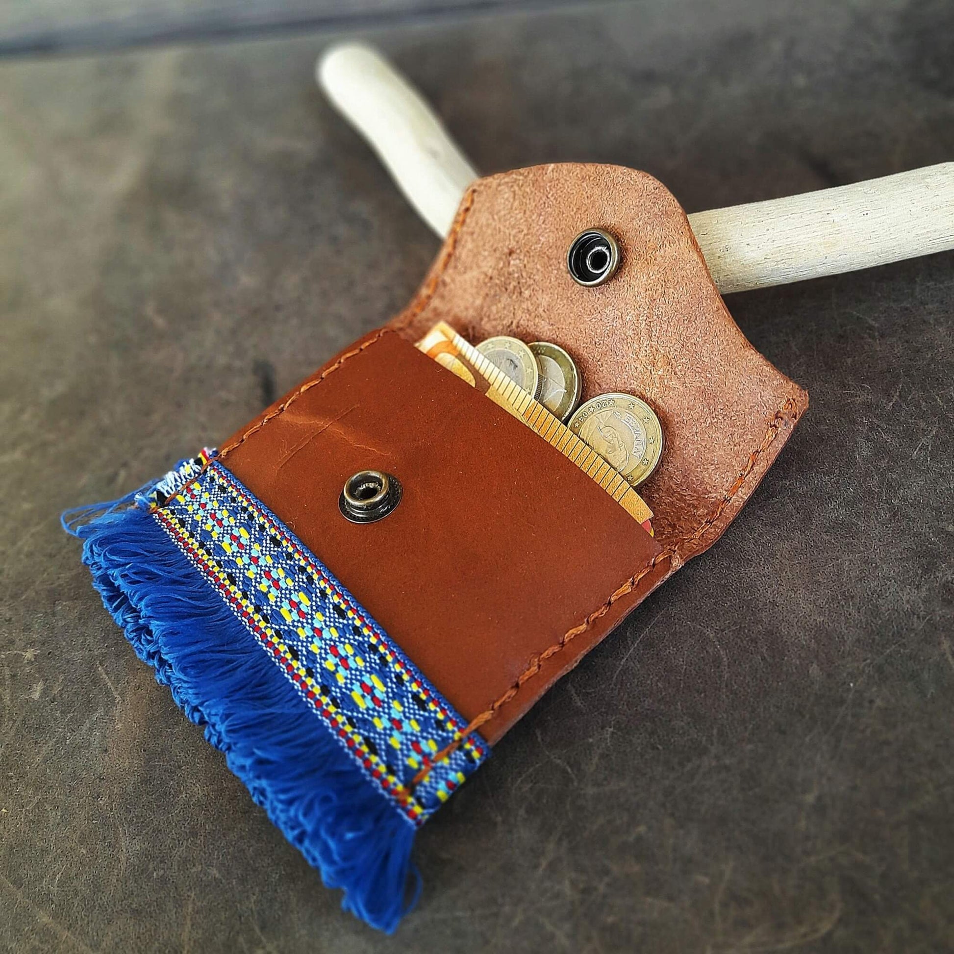 Brown leather wallet with blue fringes and coins on a dark surface