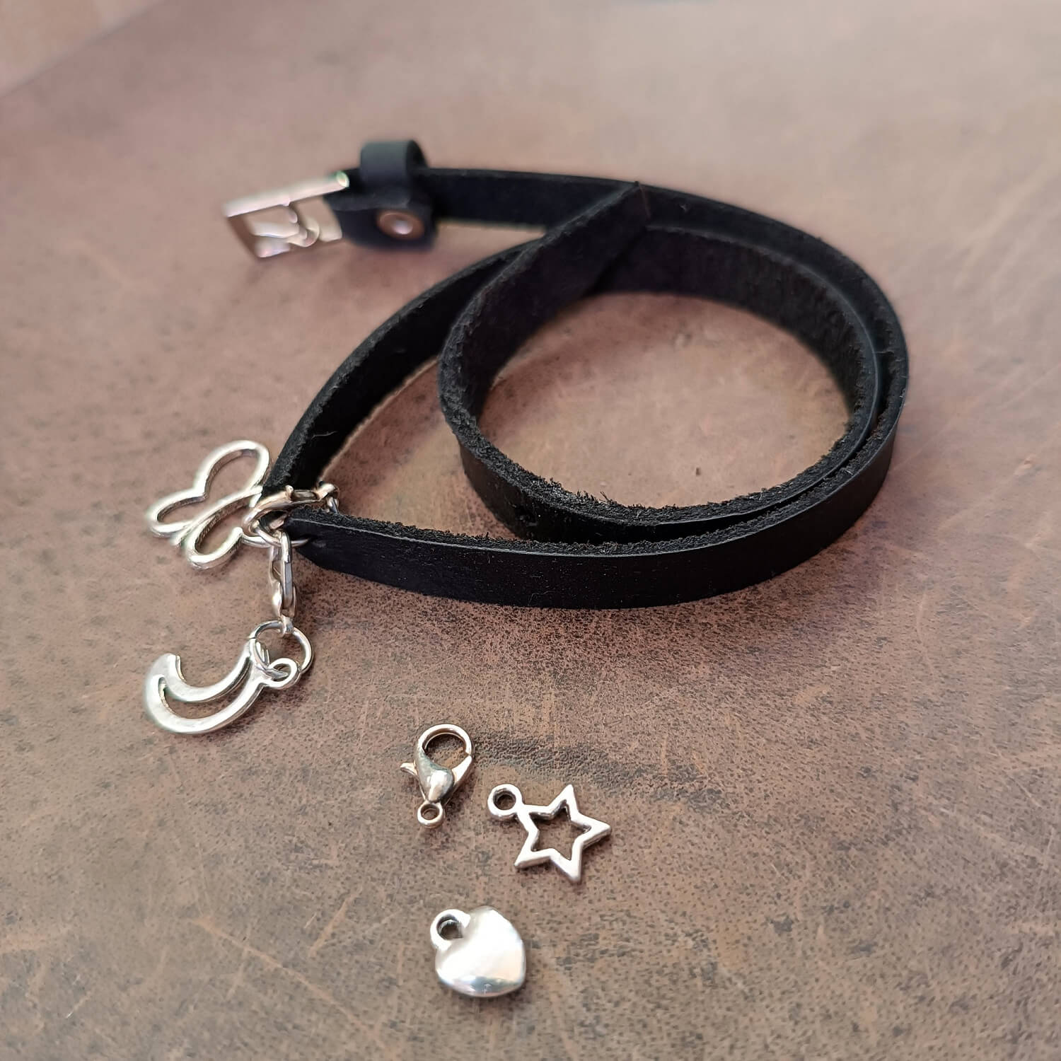 Detailed close-up of The Evolve Choker/Bracelet, highlighting the texture of the black Crazy Horse leather, the buckle, the double wrap-bracelet style and custom charms that can be attached.