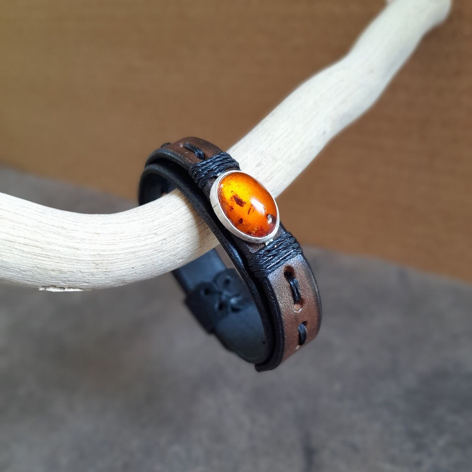 The OOAK Amber Time Capsule Bracelet: A layered black and earthy oak brown leather bracelet featuring a captivating oval natural amber cabochon on a sterling silver pendant, wrapped with black cord.