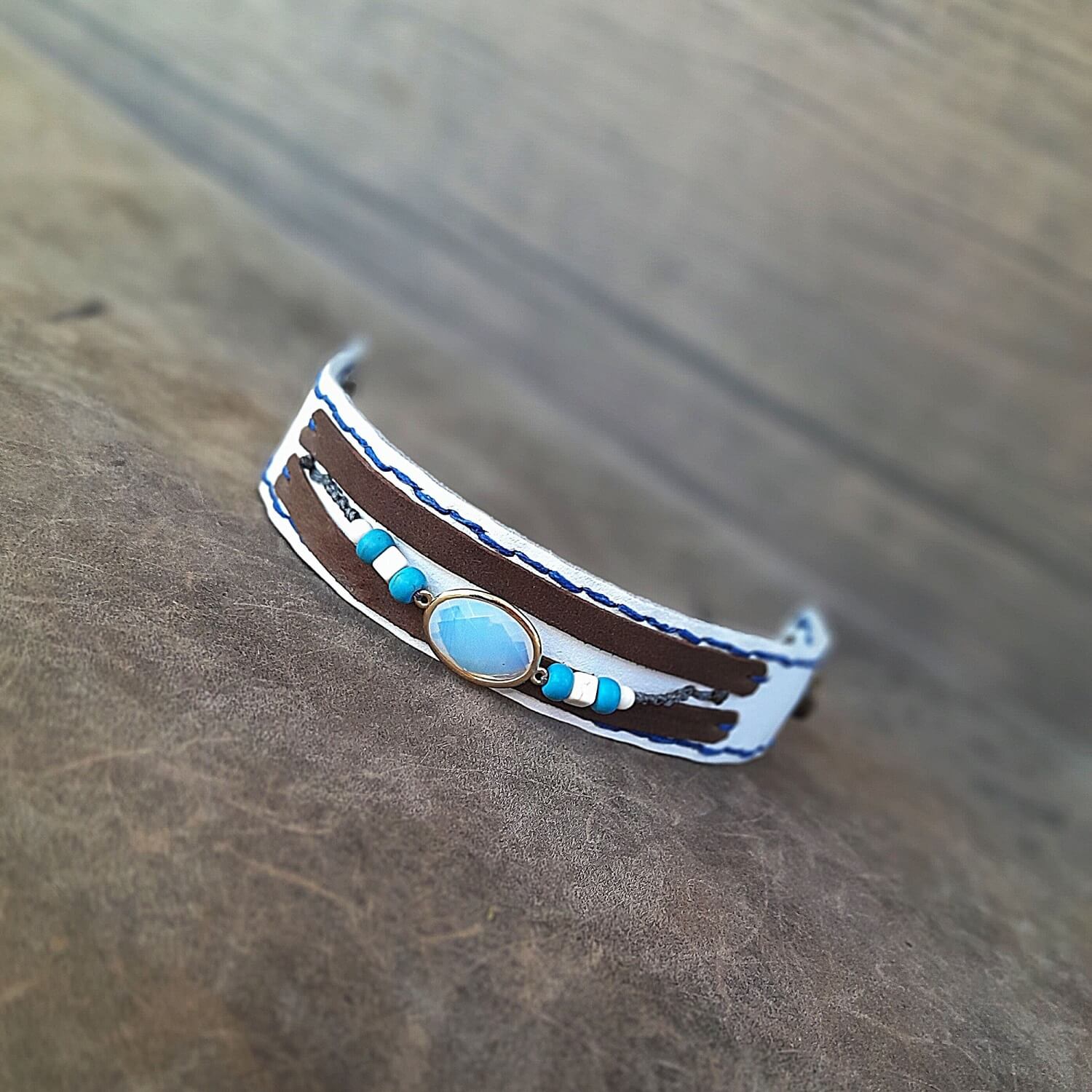 The OOAK Boho Opal Cuff. flat lay, open: A wide white full-grain leather bracelet with dark brown suede stripes, featuring an opal pendant, white howlite, and turquoise beads in discreet macramé, with two snap closures.