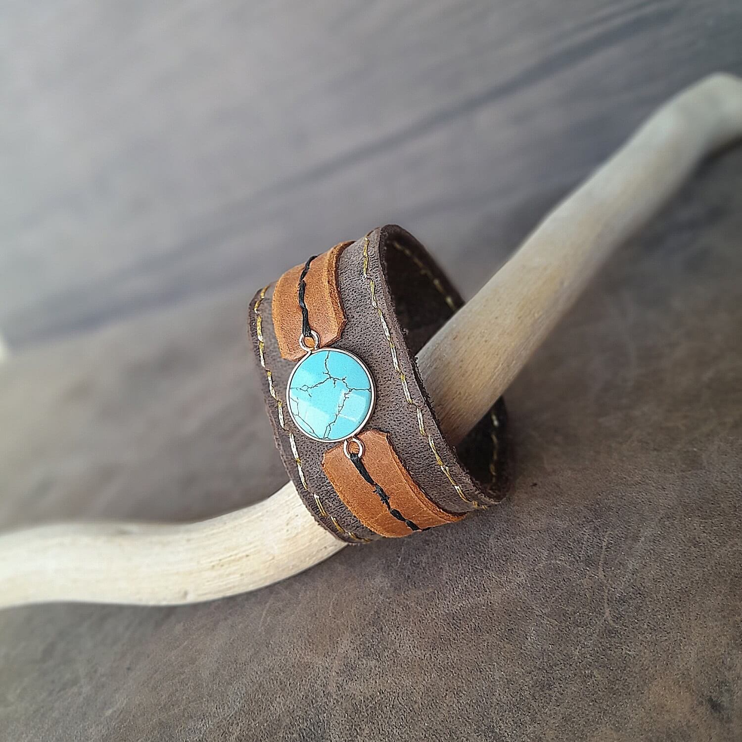 The OOAK Boho Turquoise Cuff: A wide, layered cigar gray and earthy brown full-grain leather bracelet featuring a prominent gold-plated turquoise cabochon and subtle gold stitching. Secured with antique bronze snap buttons.