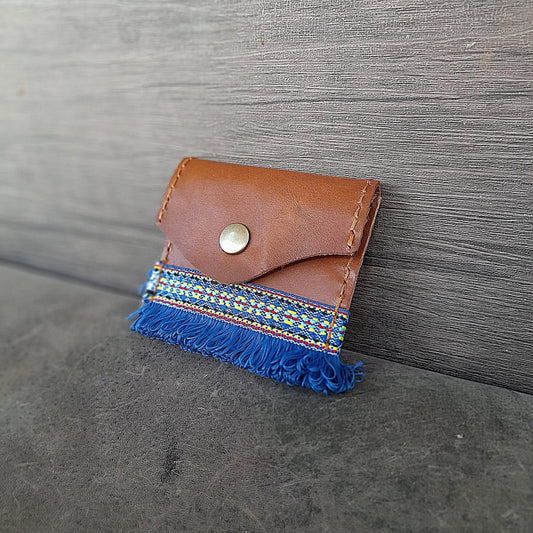 Brown leather cardholder with blue fringe on a gray surface