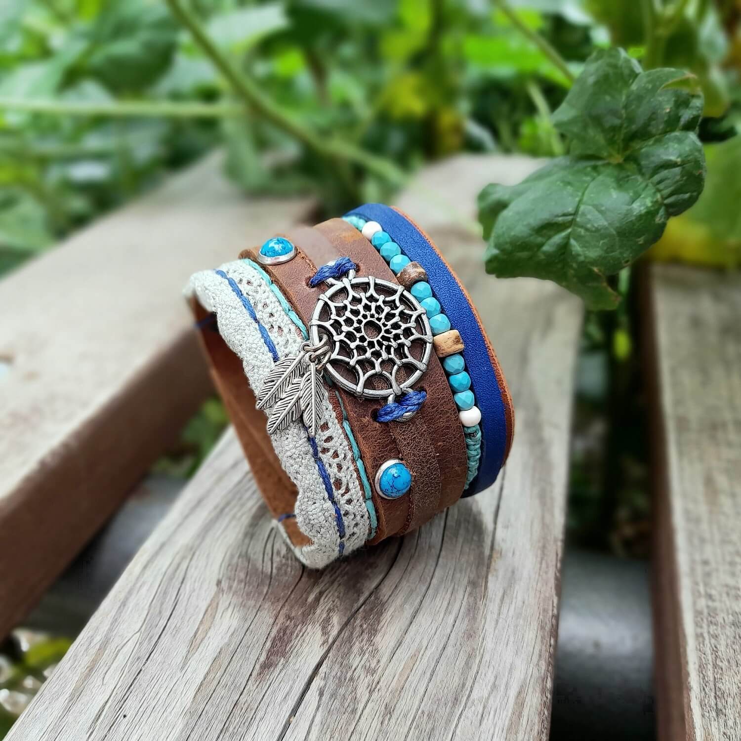 The OOAK Extra Wide Dream Catcher Boho Leather Cuff: A brown full-grain leather bracelet featuring a silver dream catcher with dangling feathers, turquoise beads, baby blue lace, and royal blue leather accents.